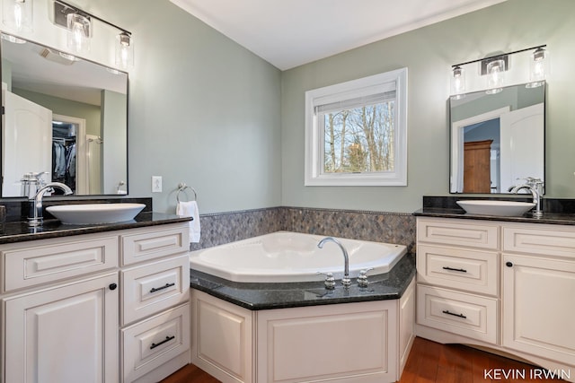 bathroom with a spacious closet, vanity, a garden tub, and wood finished floors