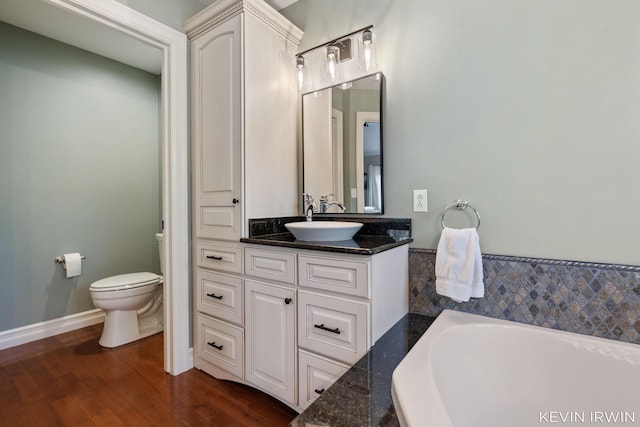 full bathroom featuring toilet, a washtub, wood finished floors, baseboards, and vanity