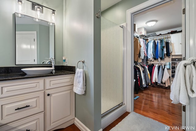 bathroom with vanity, wood finished floors, baseboards, a shower stall, and a spacious closet