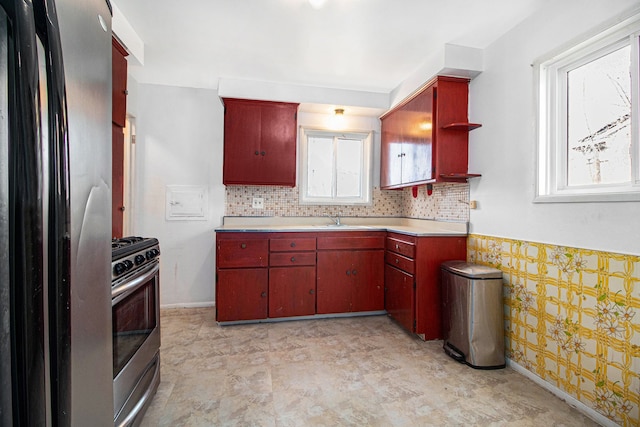 kitchen with baseboards, red cabinetry, a sink, light countertops, and appliances with stainless steel finishes