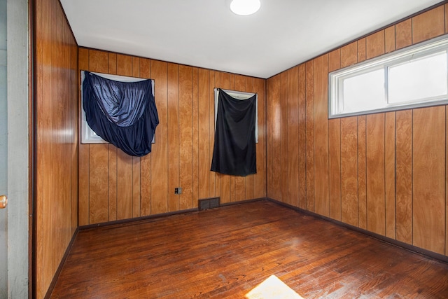 empty room featuring visible vents, baseboards, wooden walls, and hardwood / wood-style floors