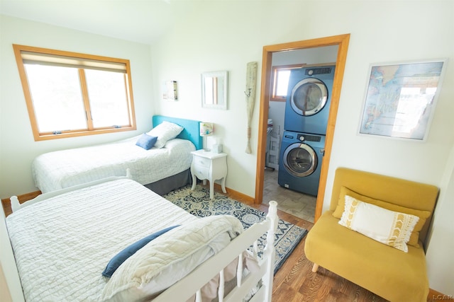 bedroom featuring baseboards, wood finished floors, and stacked washing maching and dryer