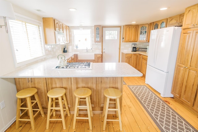 kitchen featuring tasteful backsplash, glass insert cabinets, light wood-style floors, white appliances, and a sink