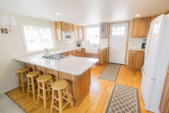 kitchen featuring a wealth of natural light, white appliances, a peninsula, and light wood-style flooring