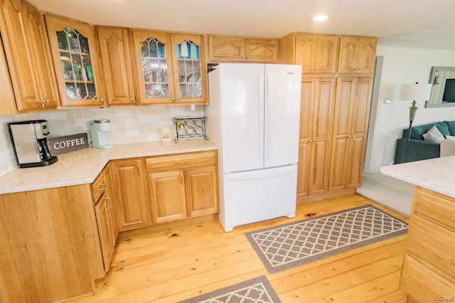 kitchen with backsplash, glass insert cabinets, light stone counters, light wood-style flooring, and freestanding refrigerator