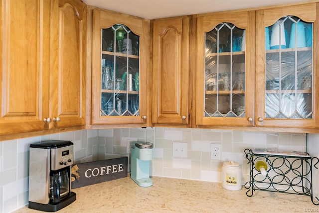 details featuring glass insert cabinets, tasteful backsplash, and light stone countertops