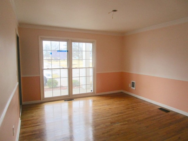 unfurnished room featuring a wealth of natural light, visible vents, crown molding, and wood finished floors