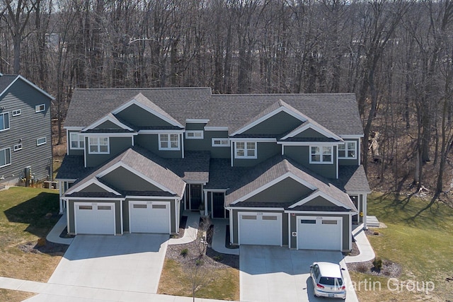 view of front of property featuring a front yard, roof with shingles, a wooded view, and driveway