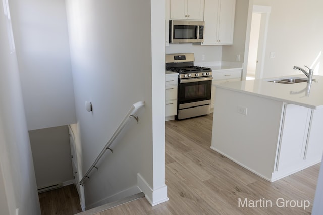 kitchen featuring a sink, light countertops, white cabinets, light wood-style floors, and appliances with stainless steel finishes