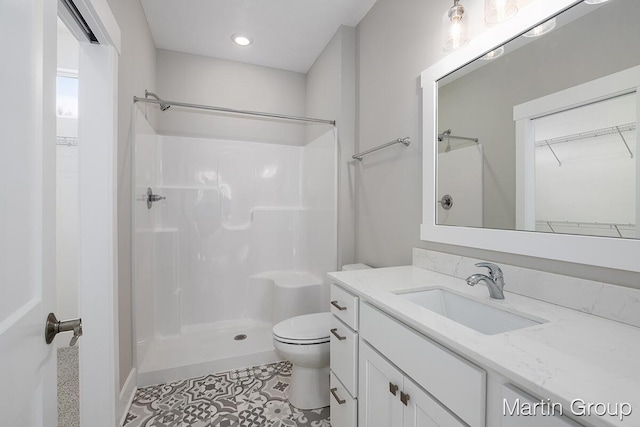 bathroom featuring a walk in closet, vanity, toilet, and a shower stall