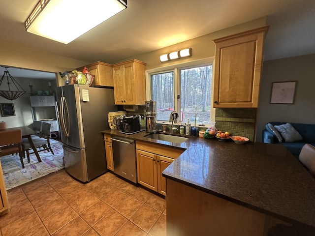 kitchen with light tile patterned floors, a sink, decorative backsplash, stainless steel appliances, and dark countertops