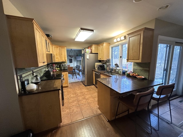 kitchen with a peninsula, a sink, stainless steel appliances, dark countertops, and backsplash