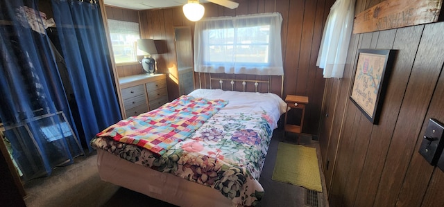 bedroom featuring multiple windows, wooden walls, and a ceiling fan