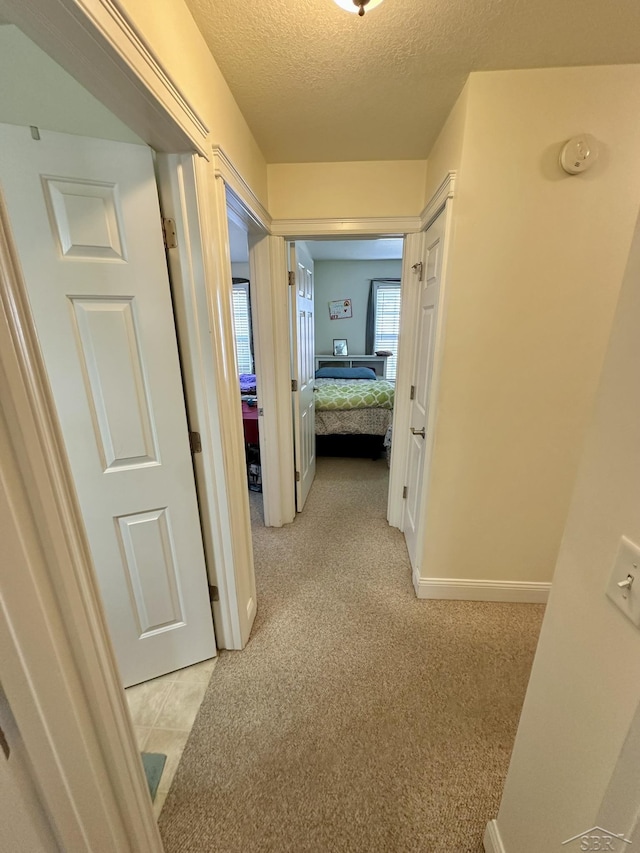 hall featuring light colored carpet, a textured ceiling, and baseboards