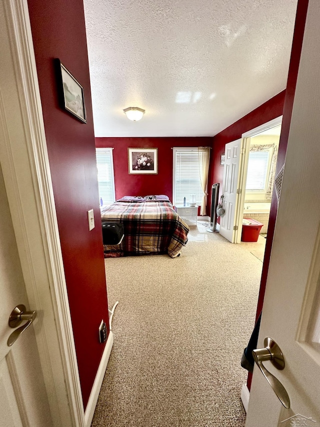 carpeted bedroom featuring a textured ceiling, ensuite bathroom, and baseboards