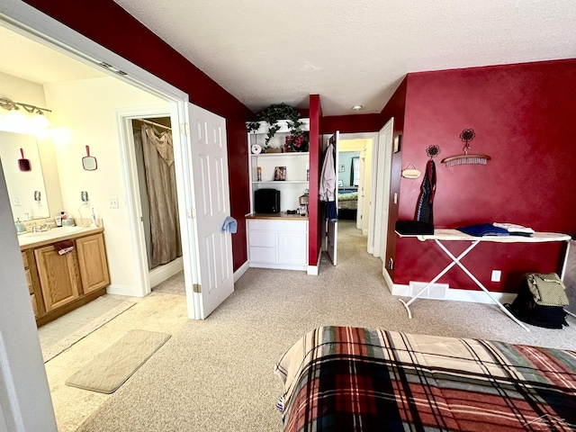 bedroom featuring light carpet, ensuite bathroom, baseboards, and a sink