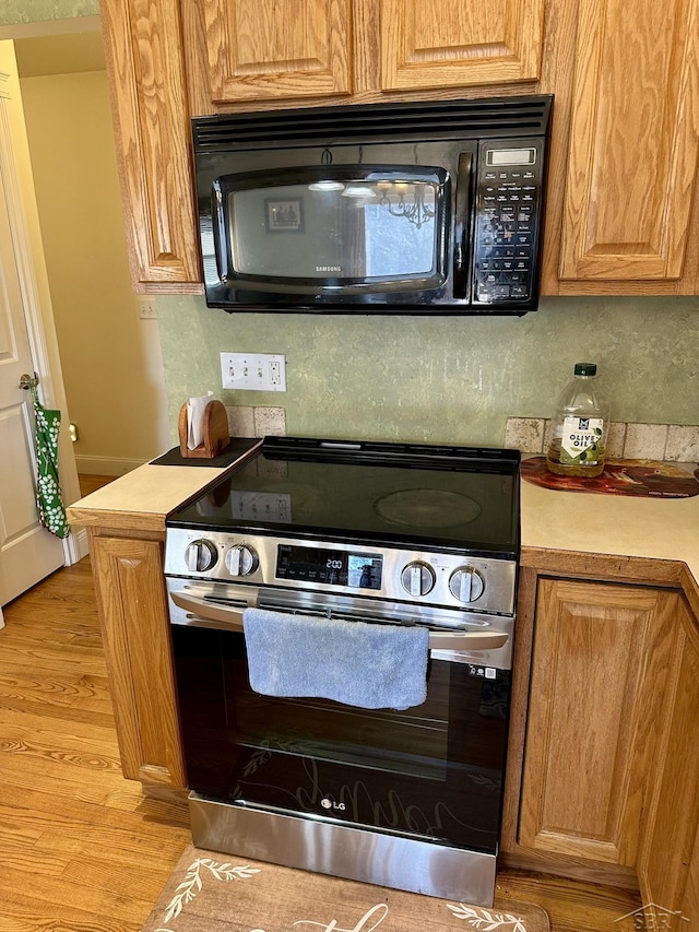 kitchen featuring light wood finished floors, tasteful backsplash, black microwave, stainless steel electric stove, and light countertops