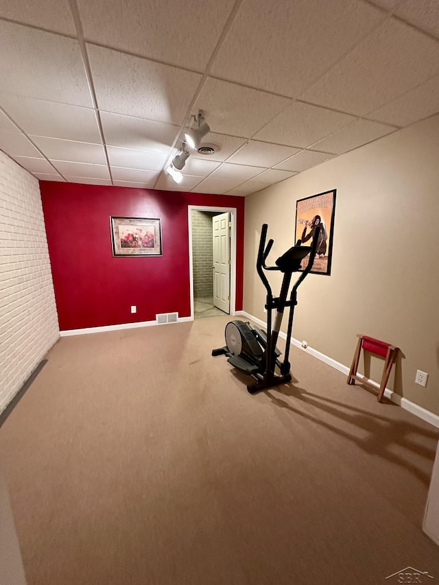 exercise area with visible vents, a drop ceiling, brick wall, carpet flooring, and baseboards