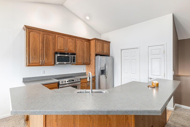 kitchen with baseboards, a sink, stainless steel appliances, vaulted ceiling, and brown cabinets