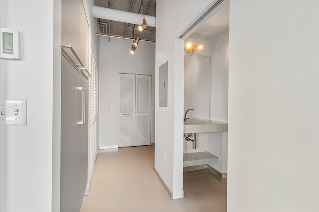 corridor featuring electric panel, baseboards, concrete floors, and a towering ceiling