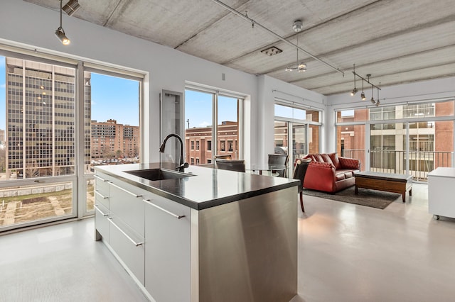 kitchen with concrete floors, open floor plan, an island with sink, white cabinets, and a sink