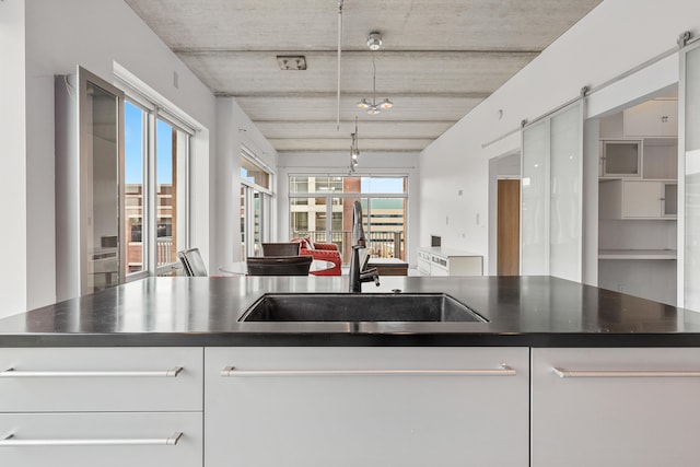 kitchen featuring dark countertops, open floor plan, a barn door, white cabinetry, and a sink