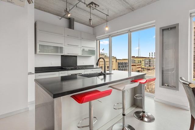 kitchen with a sink, a kitchen breakfast bar, dark countertops, and finished concrete flooring