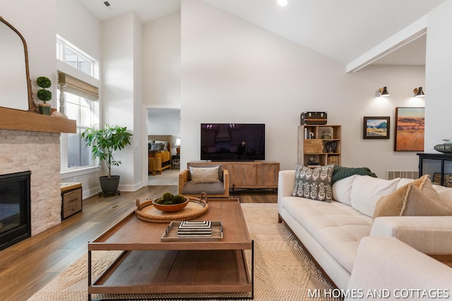 living area with baseboards, high vaulted ceiling, a stone fireplace, and wood finished floors