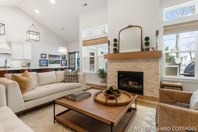 living room with light wood finished floors, visible vents, a healthy amount of sunlight, and a stone fireplace