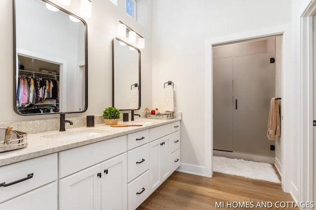 full bath featuring double vanity, wood finished floors, baseboards, and a sink