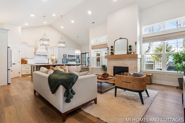 living area with a fireplace, high vaulted ceiling, light wood-type flooring, and baseboards