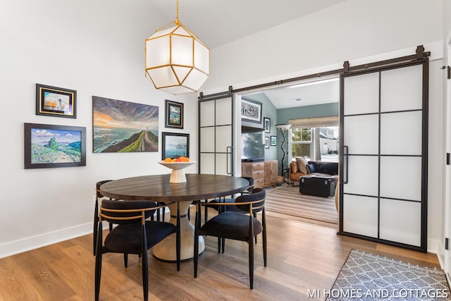 dining room featuring a barn door, baseboards, lofted ceiling, and wood finished floors