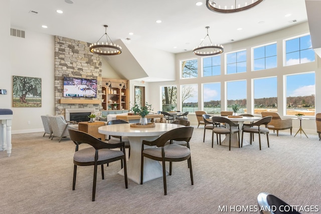 dining space with a stone fireplace, visible vents, a towering ceiling, and light carpet