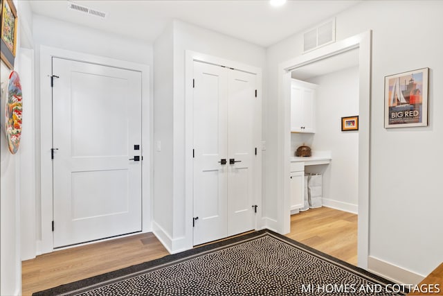 foyer entrance with light wood-style flooring, baseboards, and visible vents