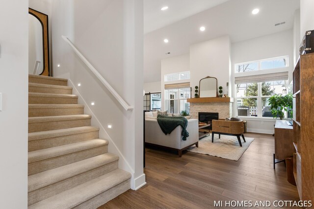 interior space featuring wood finished floors, visible vents, a high ceiling, recessed lighting, and a stone fireplace