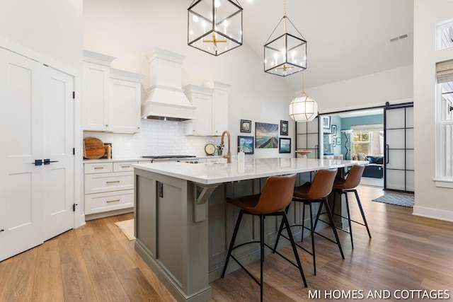 kitchen featuring visible vents, custom exhaust hood, decorative backsplash, light wood-style floors, and a barn door