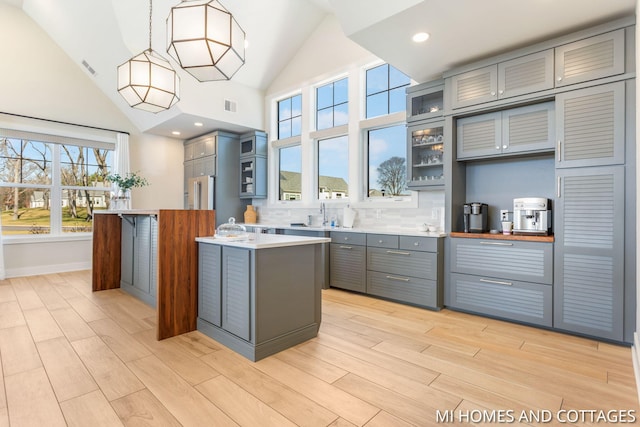 kitchen featuring visible vents, gray cabinets, tasteful backsplash, light wood-style floors, and glass insert cabinets