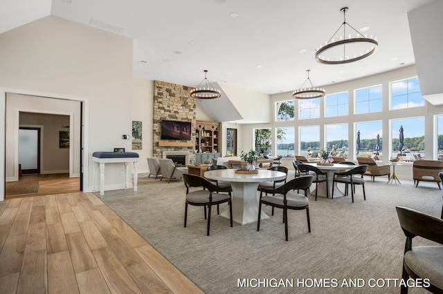 dining room featuring high vaulted ceiling, a notable chandelier, light wood-style flooring, a fireplace, and baseboards