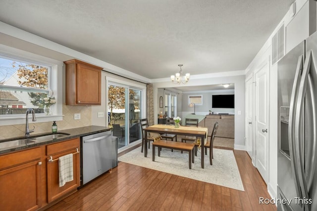 kitchen featuring dark wood-style floors, brown cabinetry, a sink, decorative backsplash, and appliances with stainless steel finishes