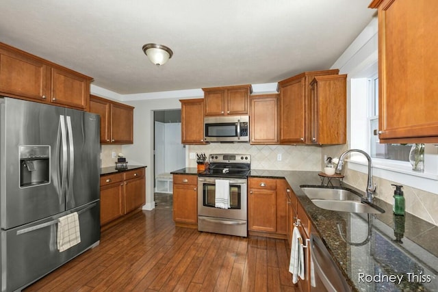 kitchen featuring brown cabinets, a sink, dark wood-style floors, stainless steel appliances, and decorative backsplash