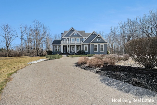 shingle-style home with a front lawn, a balcony, covered porch, and driveway