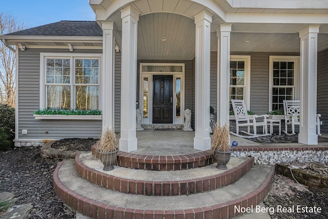 property entrance featuring covered porch and a shingled roof