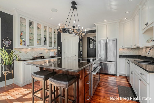 kitchen featuring a sink, premium appliances, a center island, white cabinets, and glass insert cabinets