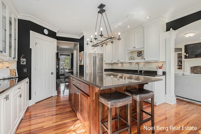 kitchen featuring light wood finished floors, a kitchen island, stainless steel refrigerator, glass insert cabinets, and dark countertops