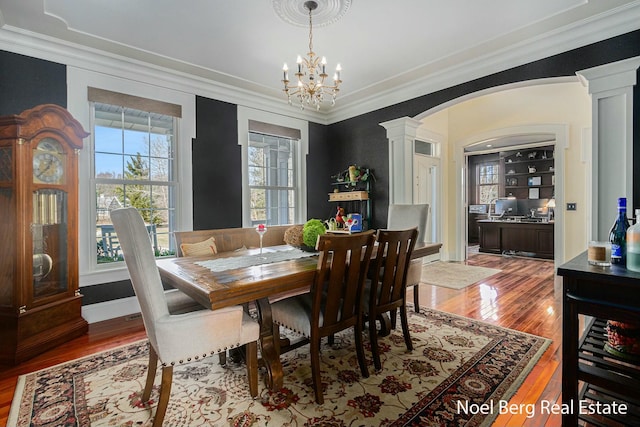 dining room featuring hardwood / wood-style floors, crown molding, decorative columns, and arched walkways