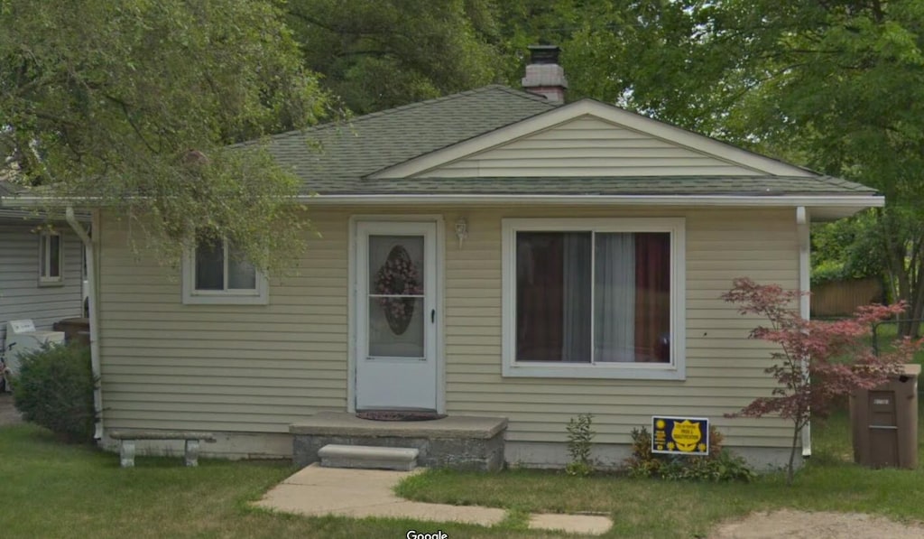 bungalow-style house with a chimney, a shingled roof, and a front lawn