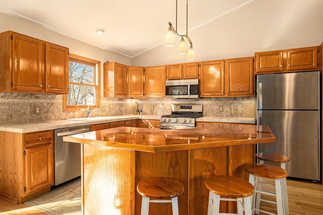 kitchen featuring stainless steel appliances, decorative backsplash, vaulted ceiling, brown cabinets, and a center island