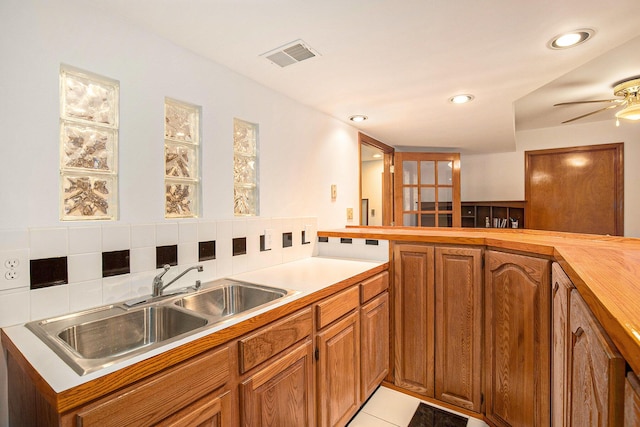 kitchen with light tile patterned floors, visible vents, a sink, brown cabinets, and backsplash