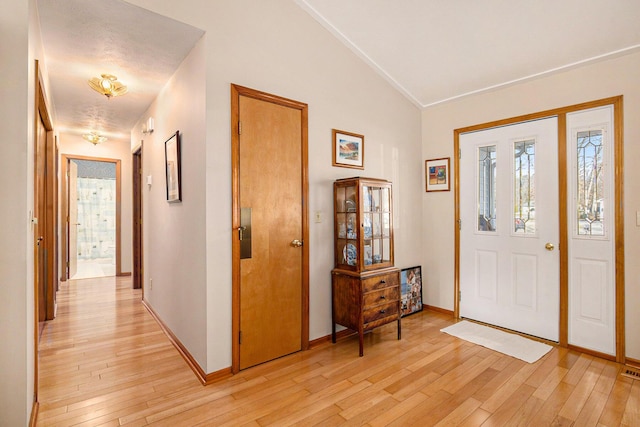 foyer entrance with light wood-type flooring, baseboards, and vaulted ceiling