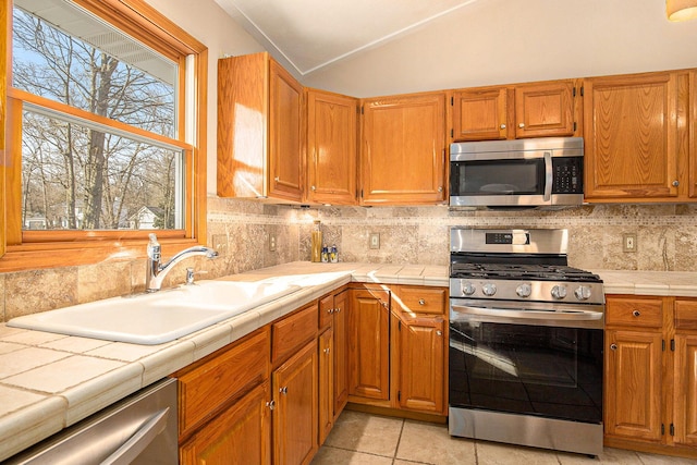 kitchen featuring a sink, appliances with stainless steel finishes, tile counters, and vaulted ceiling